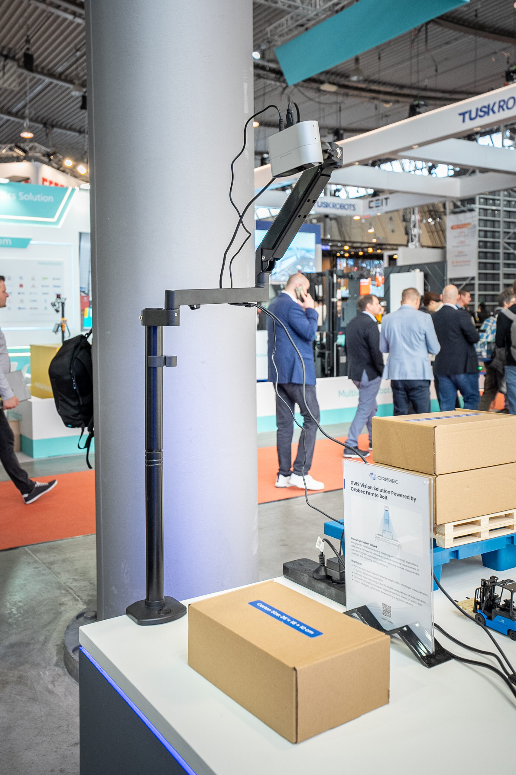 Orbbec Femto Bolt ToF camera mounted on stand demonstrating DWS dimensioning weighing and sorting vision solution with cardboard boxes at LogiMAT 2026