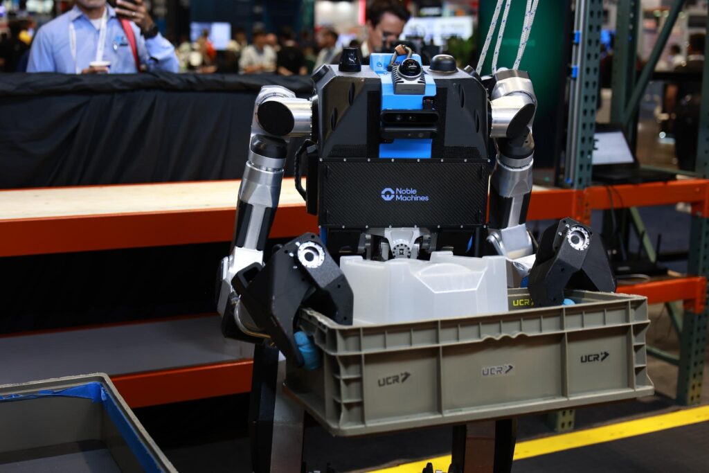 Noble Machines Moby general-purpose humanoid robot carrying a plastic storage container during industrial material handling task demonstration